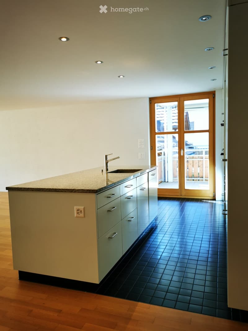 Spacious kitchen with wooden cabinets, granite countertops, and a large window overlooking a balcony or terrace. The kitchen features a sink and faucet, as well as recessed lighting in the ceiling.