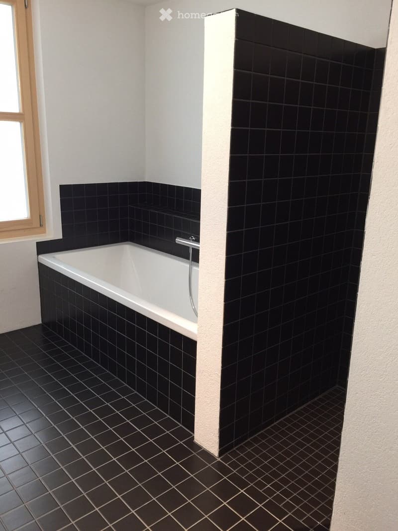 Large black tiled bathroom with a white bathtub, tiled walls and floors