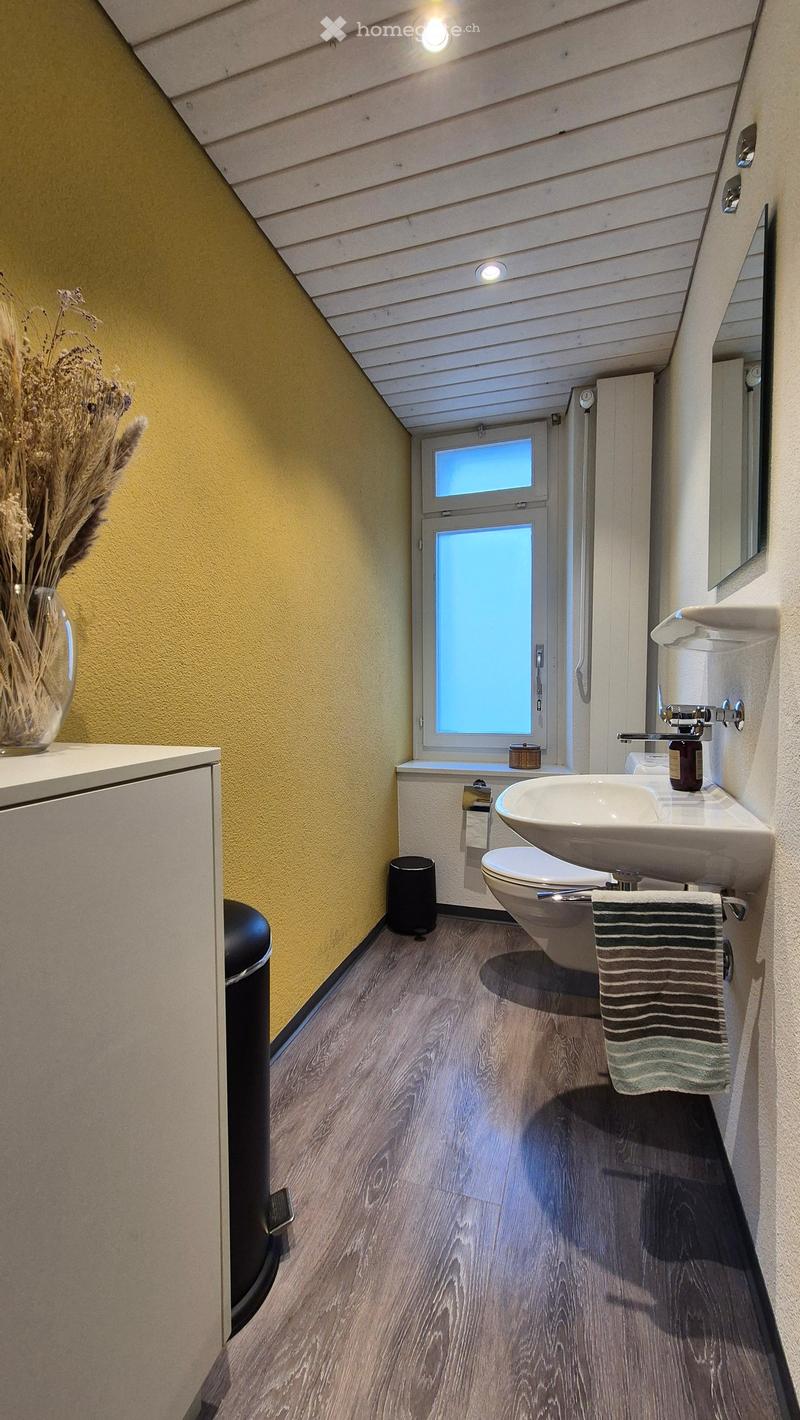 Bathroom with yellow walls, wooden floor, vanity sink, and a window. There is a washing machine visible in the room.