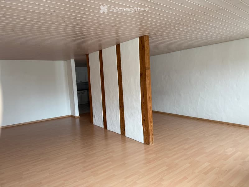empty room, wooden floor, white walls, wooden beams, kitchen in the background