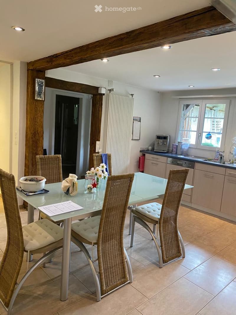 Table with chairs, wooden beams on ceiling, white tiled floor, dishwasher, window