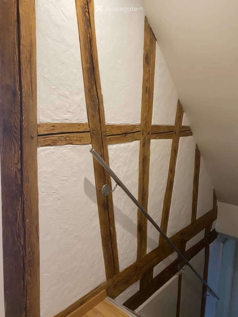 Exposed wooden beams, whitewashed walls, wooden stairs, stainless steel handrail