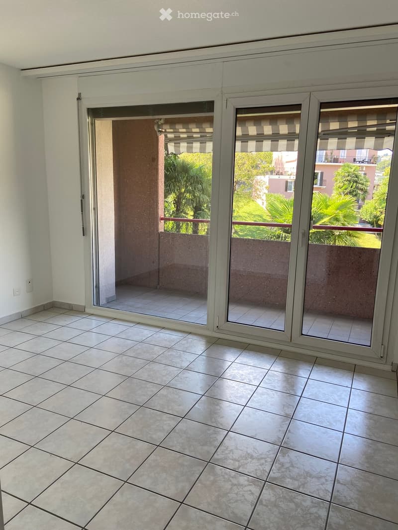 white walls, white tile floor, glass sliding doors, balcony with metal railing, outside view of plants and buildings