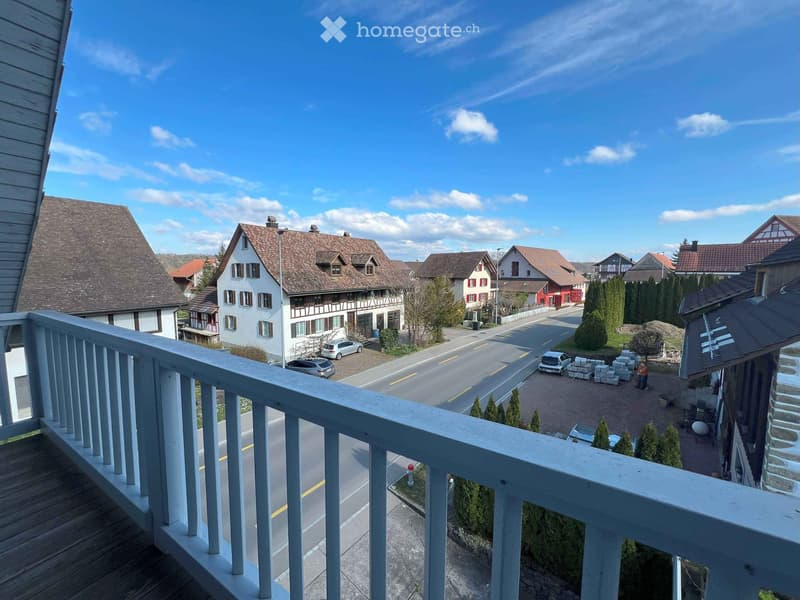 wooden balcony, cars parked on street, houses, blue sky with clouds