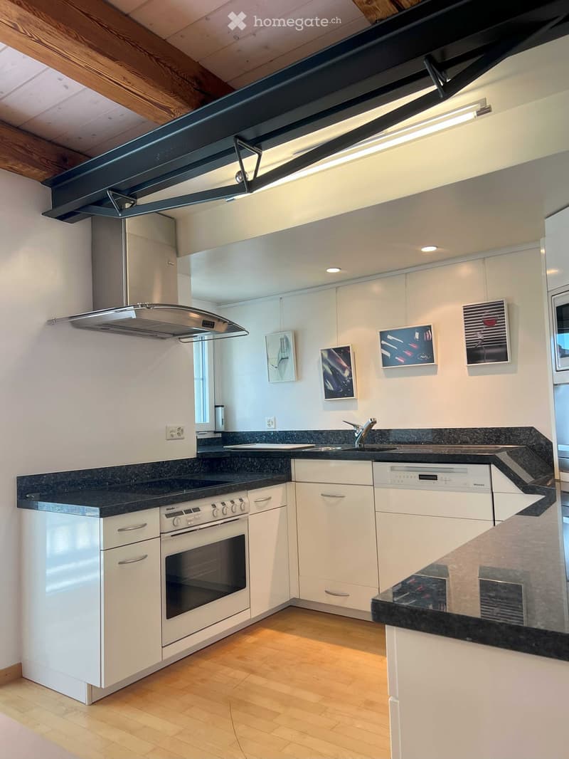 Modern white kitchen with wooden cabinets, granite countertops, stainless steel range hood, gas stove, dishwasher, and an oven with an oven door ajar. The walls are painted white, with picture frames hanging above the cabinets, and the ceiling features a