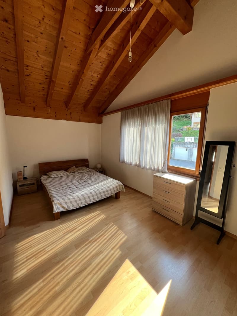 Wooden beams ceiling, wooden floor, double bed, two pillows, night lamps, small desk with lamp, wooden cabinet with drawers, mirror, window with curtain