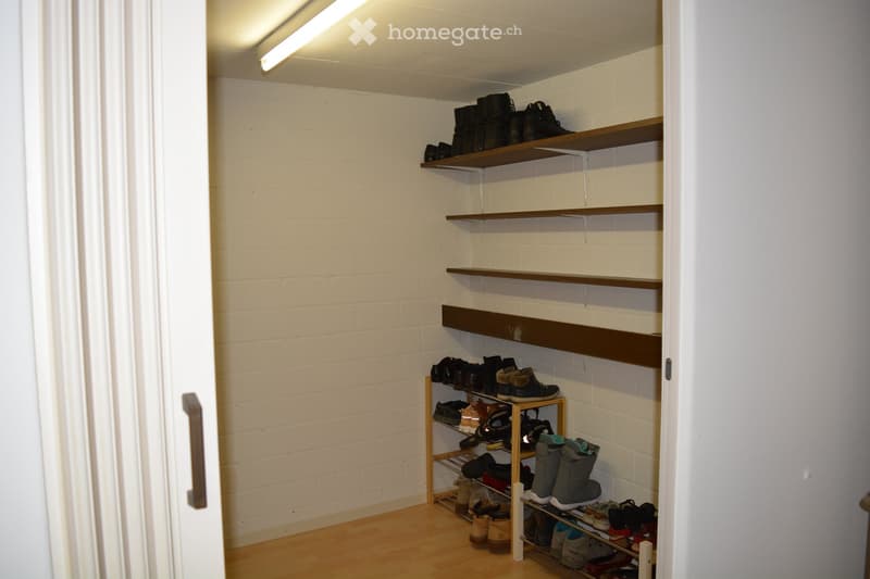 A storage closet with wooden shelves, brick walls, a metal bar, and a shoe rack.