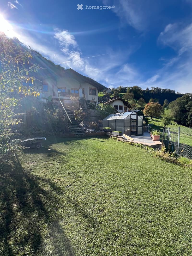 house on slope, stairs, outdoor plants, terrace, greenhouse, lawn, fenced area, clear blue sky, distant buildings