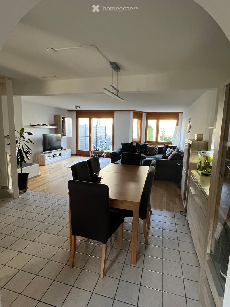 Wooden floor, white walls, wooden table, 6 black chairs, couch, shelves with TV, cabinet, aquarium