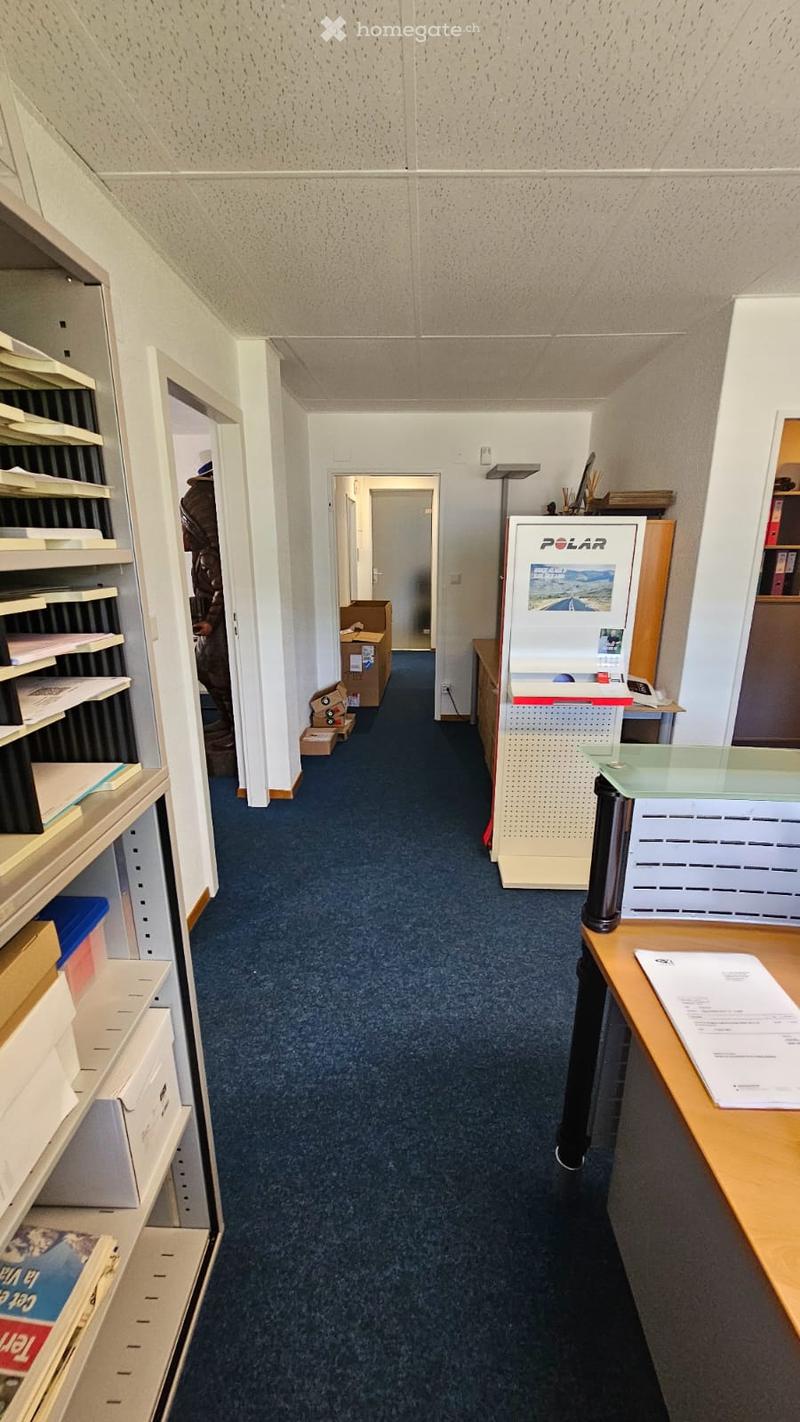 empty office, blue carpet, ceiling lights, empty office space, white walls, boxes and storage on one side, wooden desk on the right side, shelf