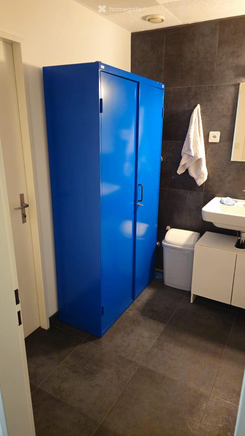 Bathroom with blue storage cabinet, white sink, white cabinet, white trash bin, towel on wall, tiled floor