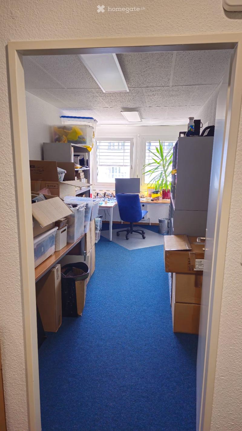 A room with boxes, cabinets, desk, chair, potted plant