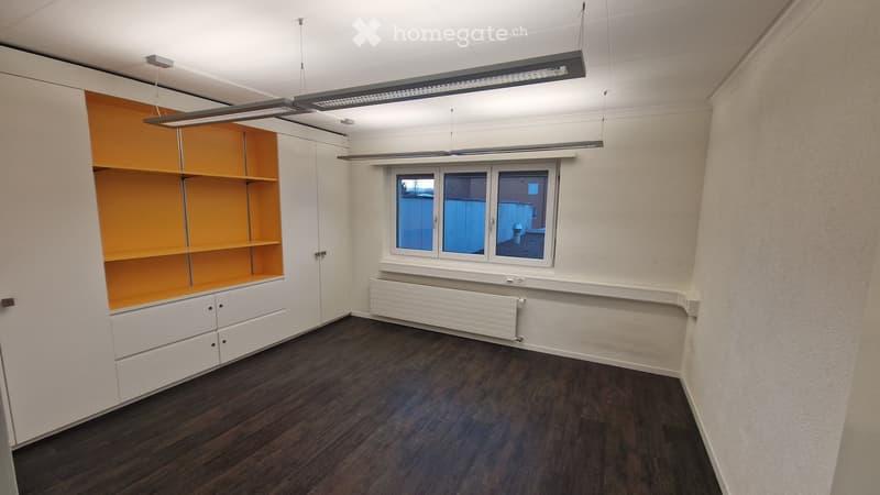 modern office room with white cabinets, orange shelves, radiator, wooden floors, window, white walls