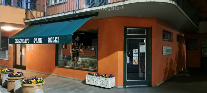 Small building with an awning, storefront window, and entrance door, with potted plants outside.