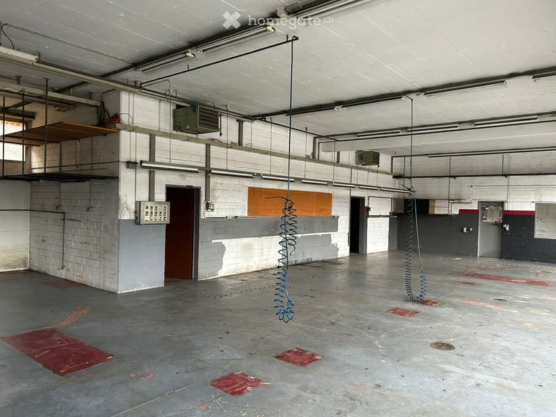 An empty warehouse with white brick walls, gray ceilings, red flooring, suspended metal springs, and several industrial lamps mounted on the ceiling.