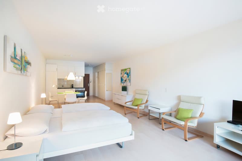 modern bedroom with double bed, two armchairs, round table, kitchen, wall art, lamp, TV, side table