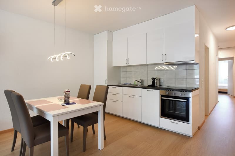 white cabinets, white tile backsplash, stainless steel gas stove, dishwasher, wooden floors, table, 4 chairs