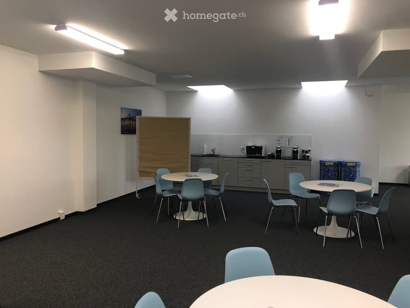 modern conference room with white walls, white tables, blue chairs, fluorescent lighting, kitchen area with microwave, coffee maker and cabinets