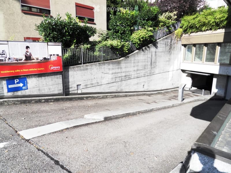 A concrete wall with a railing leads to an underground parking entrance, labeled 'P' for parking.