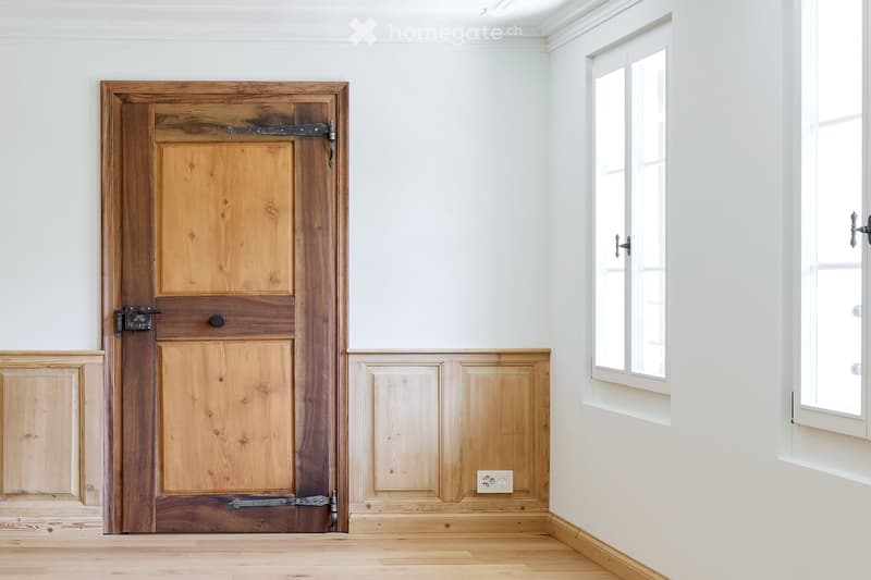 Empty room with wooden door, white walls, and hardwood floor