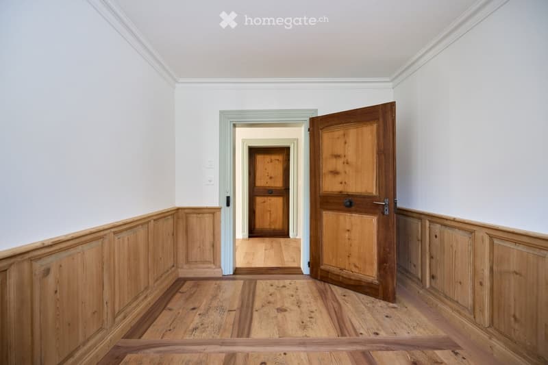 Hardwood floors, wooden paneled walls, open door leading to another room