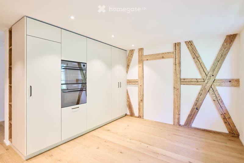 Modern white kitchen with wooden beams, wooden floor, integrated oven, multiple white cabinets