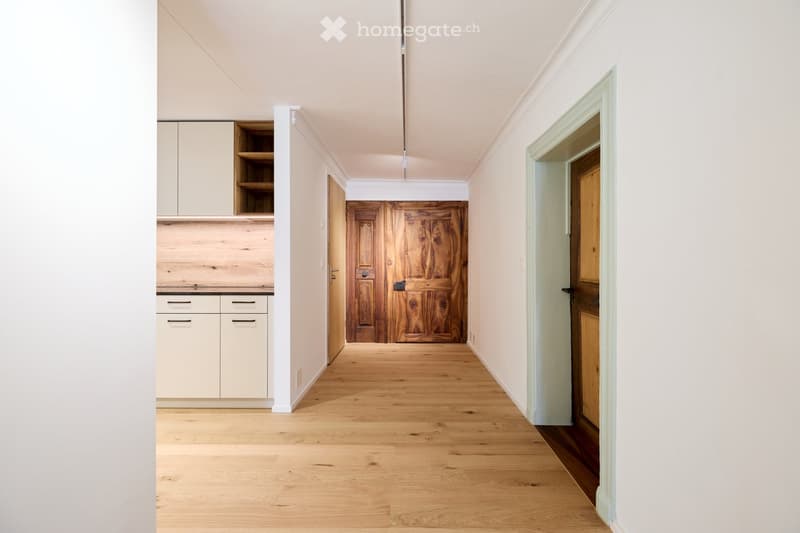 Empty hallway with wooden flooring, white walls, wooden door, white cabinets, open ceiling