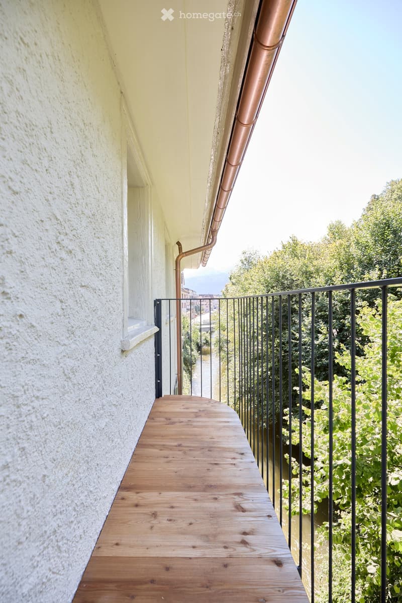 wooden terrace, black metal railing, white wall, trees