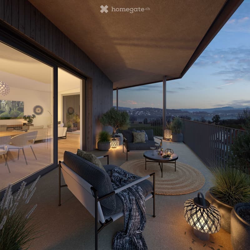 Outdoor terrace with wooden flooring, glass sliding doors, a couch with pillows, a table with decorative items, potted plants, a rug, and lamps, offering a view of a mountain and landscape