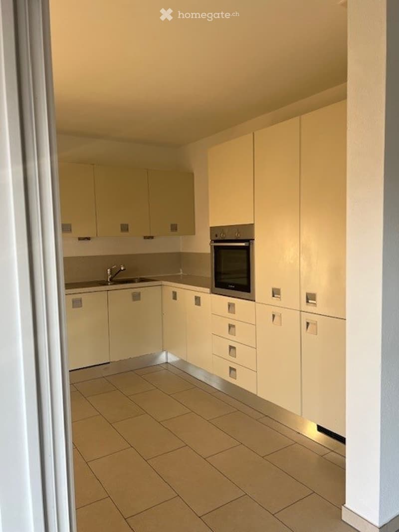 Modern fitted kitchen with tiled floor, light-colored cabinets, integrated appliances, and a stainless steel sink.