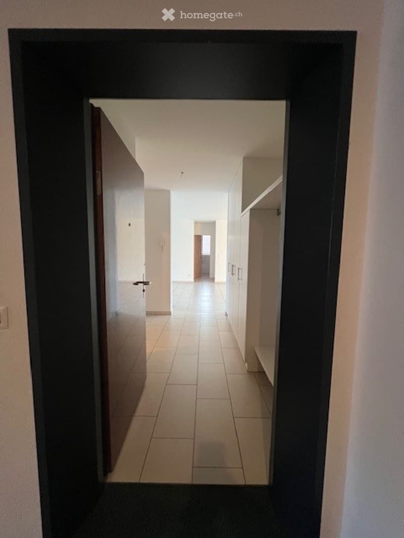 White tiled floor, white walls, wooden door, wall cabinets
