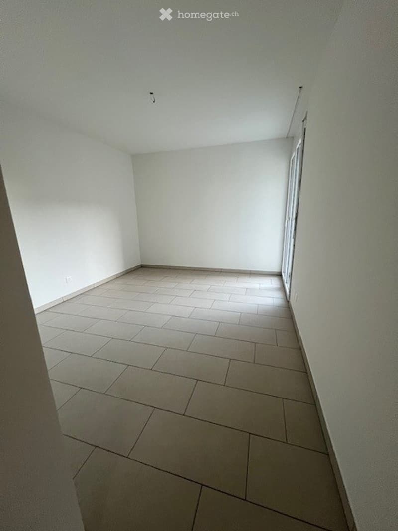 The room has white walls and a tiled floor. There is a power outlet on the wall near the corner.