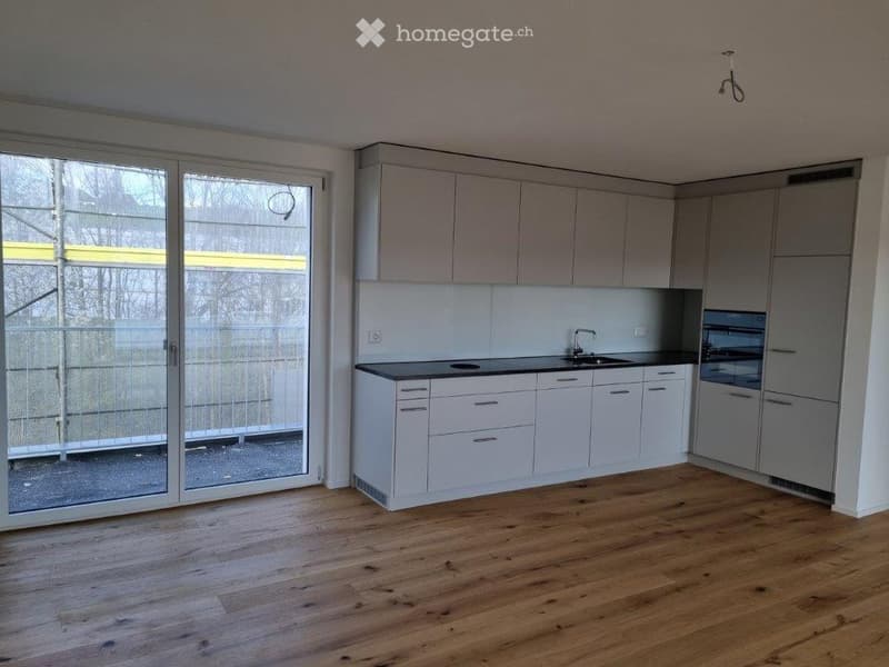 Empty kitchen with white cabinets, black countertops, stainless steel sink, and sliding glass doors leading to a balcony