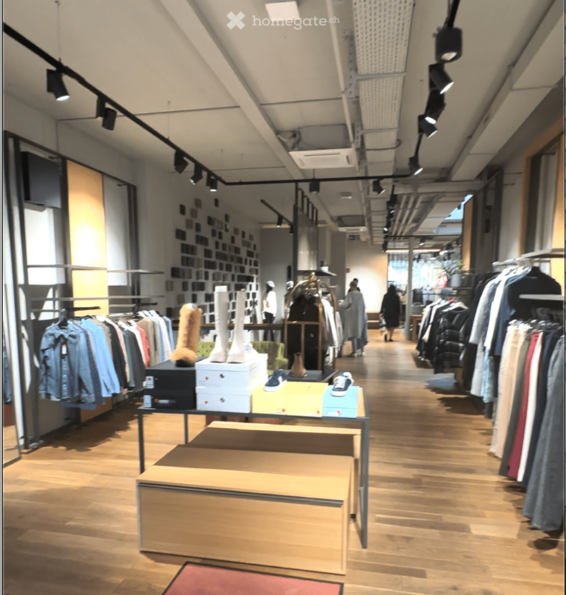 large open space with rows of clothing on hangers, display tables with shoes and boots, ceiling spotlights, wooden floors