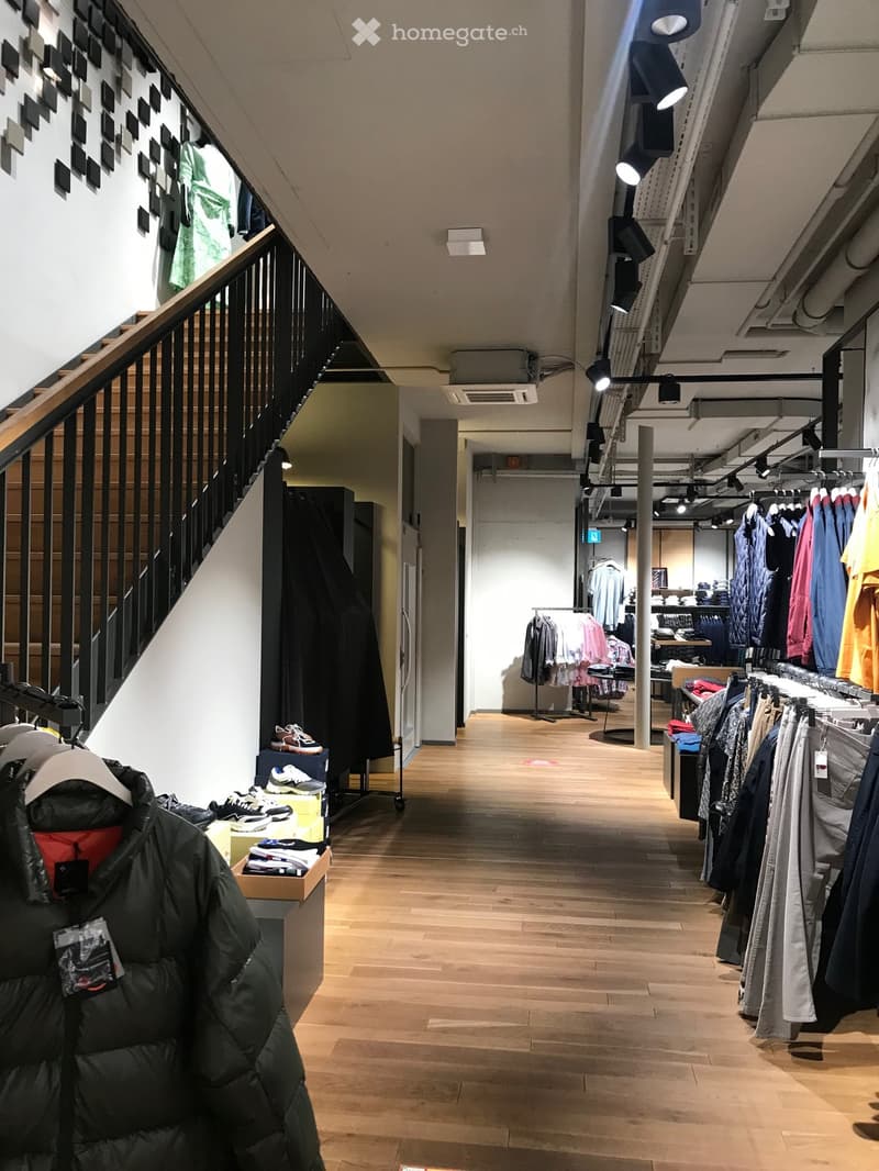 wooden flooring, a staircase, racks of clothes, shelves with products