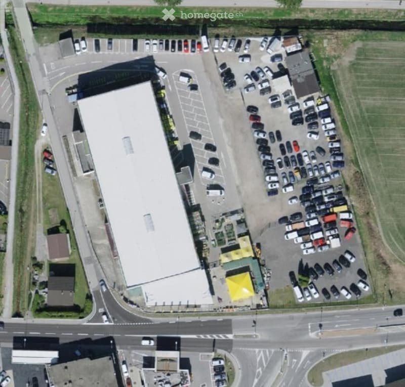 Aerial view of a building complex with a large white building and a surrounding parking area with many cars parked.