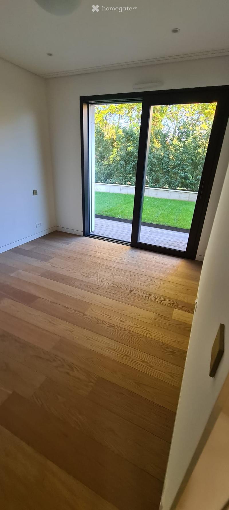 large empty room, wooden floor, sliding doors, balcony with deck, view of garden