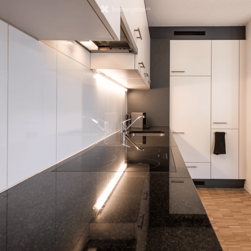 modern kitchen, black granite countertop, induction cooktop, silver faucet, white cabinetry, white tile wall, wooden flooring