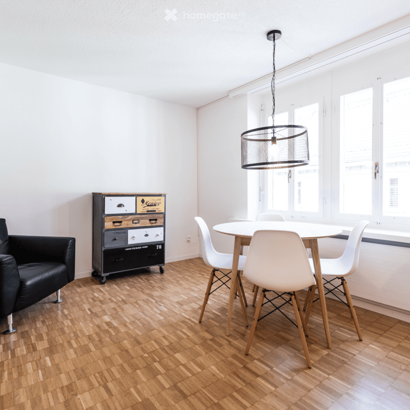 room with white walls, wooden floor, black leather sofa, white cabinet, 4 white chairs around round table, pendant light, double window