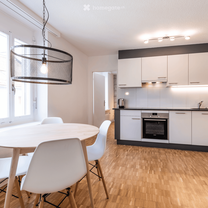 a modern kitchen with a dining table, 4 white chairs, white wooden floor, modern lights, white cabinets, modern oven and sink