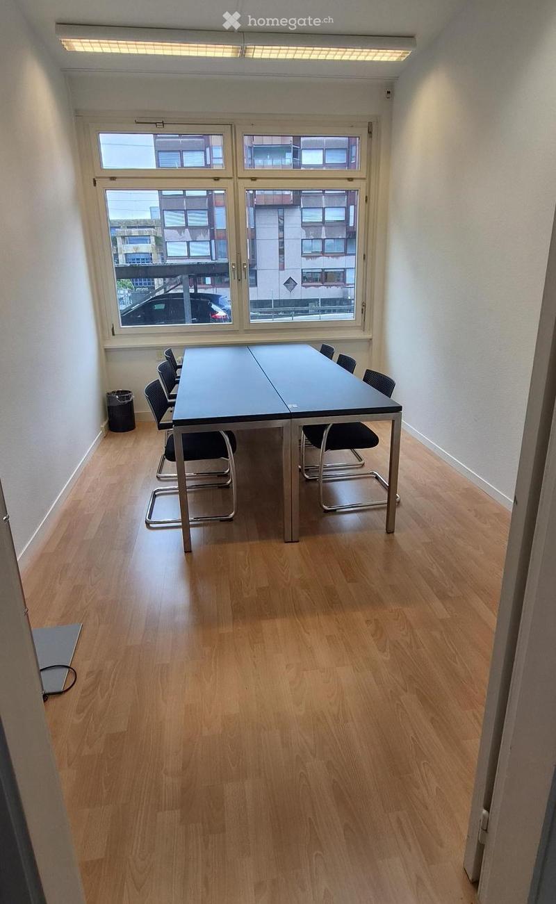 A small, unfurnished room with wooden flooring, large windows, a table, and chairs.