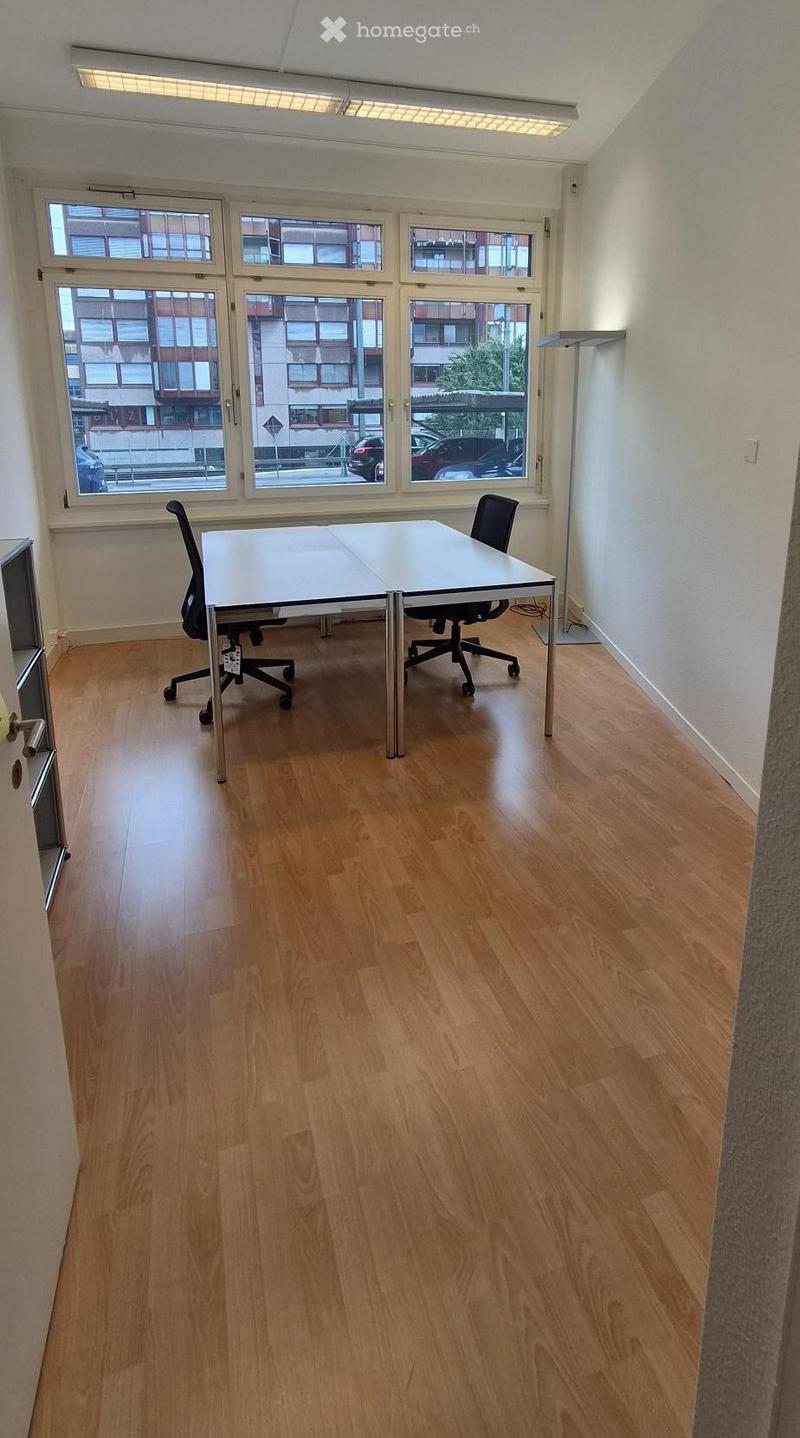 Bright, unfurnished room with wooden flooring, large windows, and a single table with two chairs.