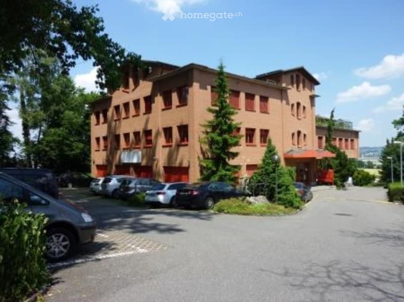 2 story brown brick building with many windows, parking lot
