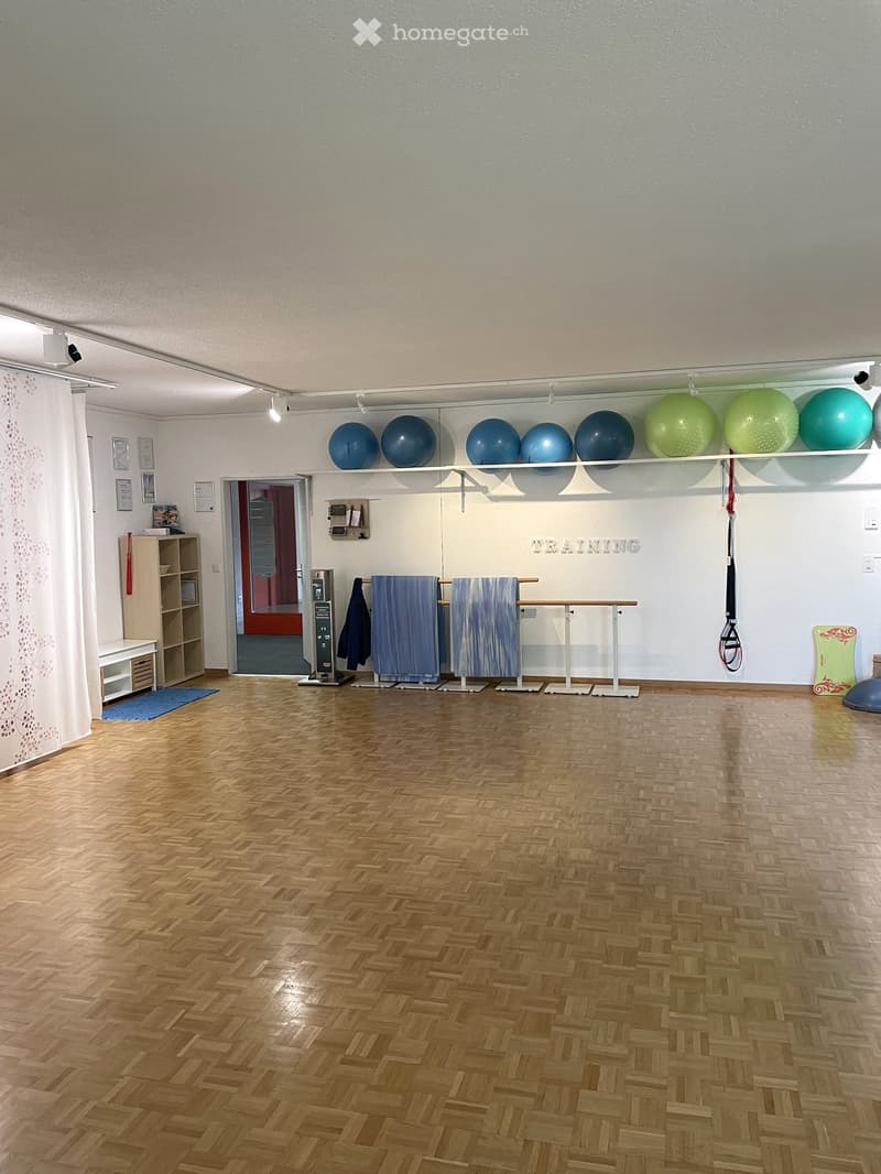 An empty room with wooden floors, various exercise equipment, including resistance bands and exercise balls, mounted on a white wall, shelves, and a wooden cabinet.