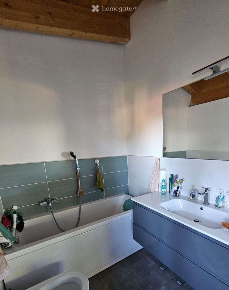 Bathroom: white bathtub, shower head, sink, mirror, wooden ceiling, tile walls
