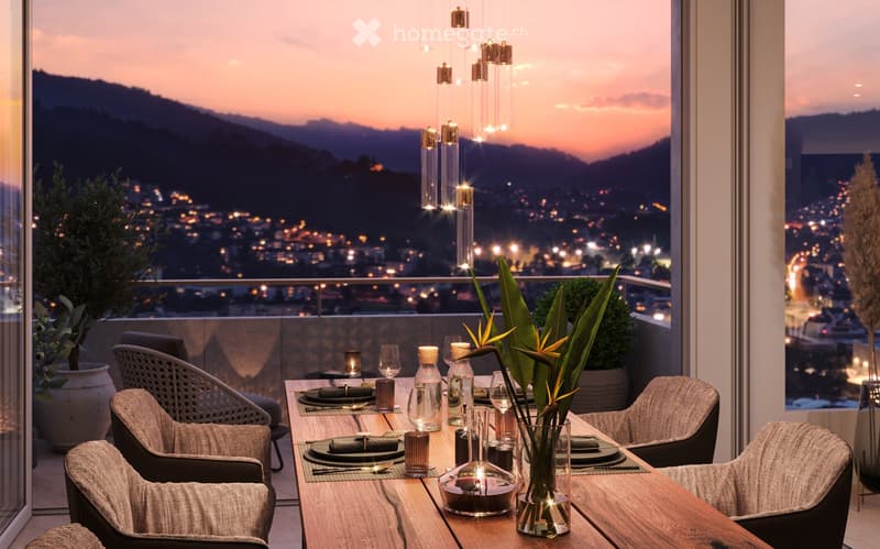 Dining table set with plates, glasses, and candles, overlooking a scenic night view of a city with mountains in the background. The room has large windows and modern lighting fixtures.