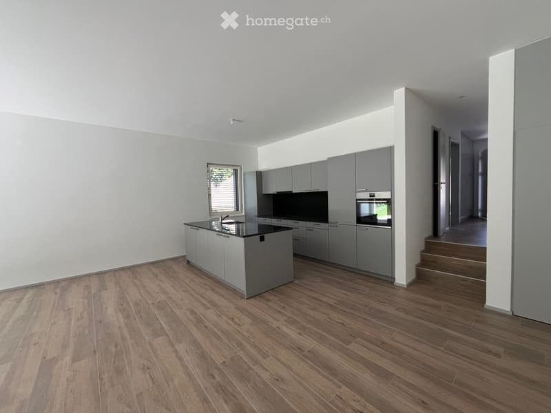 Modern kitchen with light grey cabinets, a central island, and a black countertop. The floor is made of light wood, and there is a window with blinds on the left side.