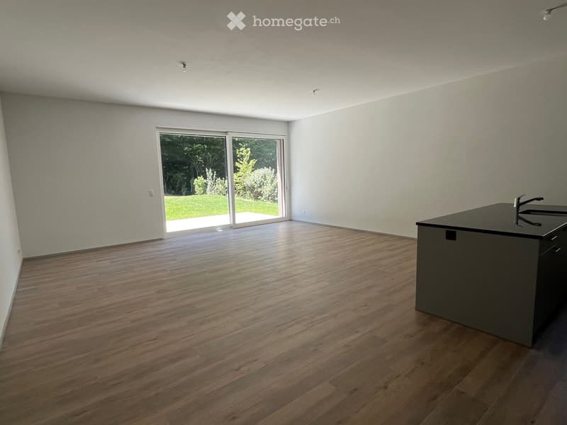 Empty room with wooden flooring, white walls, and a sliding glass door leading to a green outdoor area. A small black countertop with a faucet is visible on the right side.