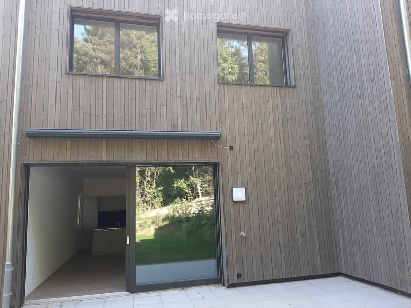 Modern house exterior with wooden siding, large windows, and a sliding glass door leading to an interior space.
