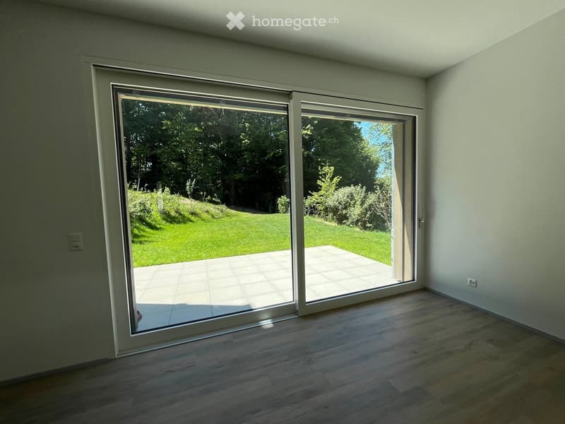 Empty room with wooden flooring and large sliding glass doors opening to a tiled patio and green lawn.